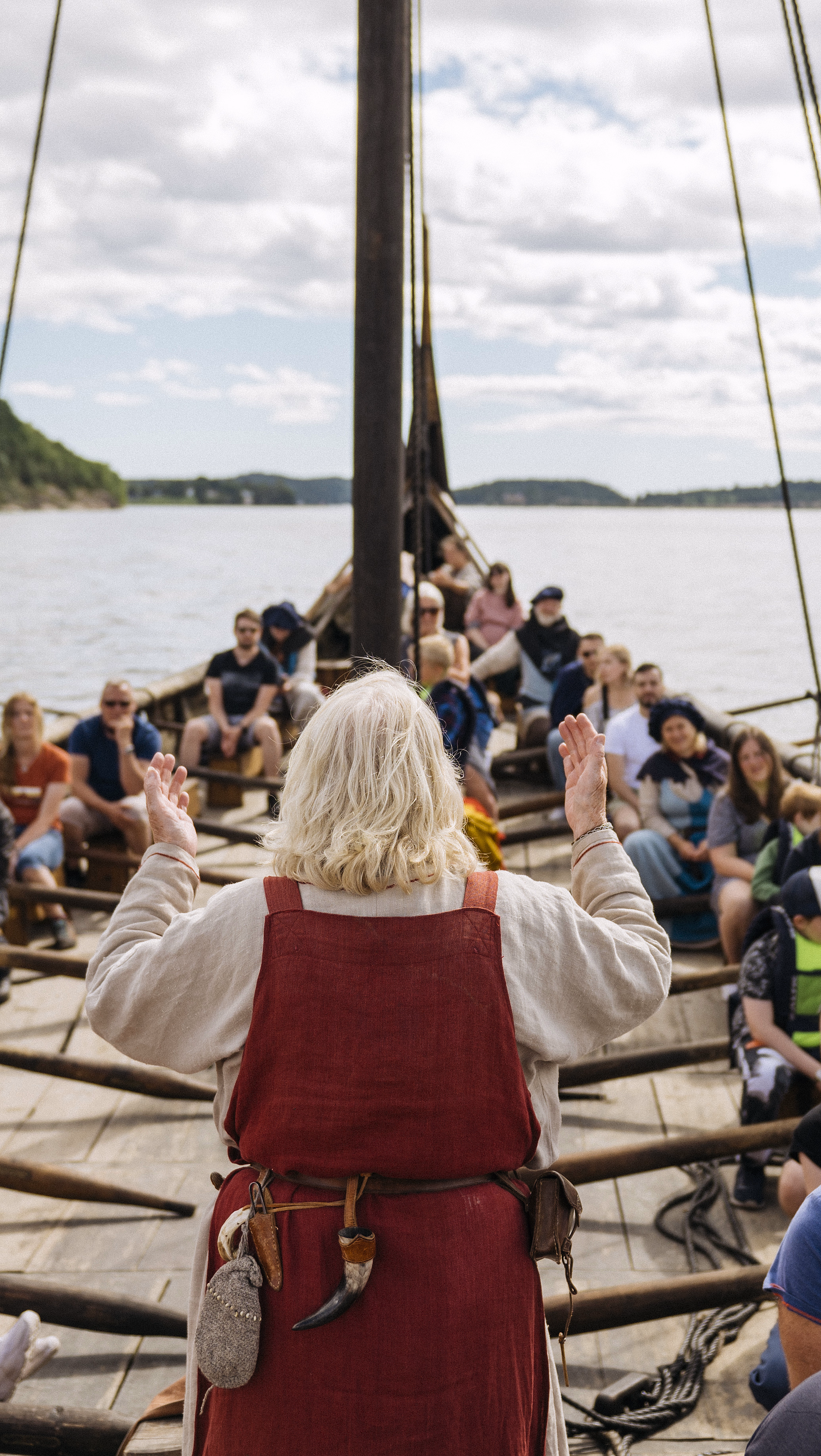 Person med hvitt hår står foran en gruppe i en trebåt med årer på vannet
