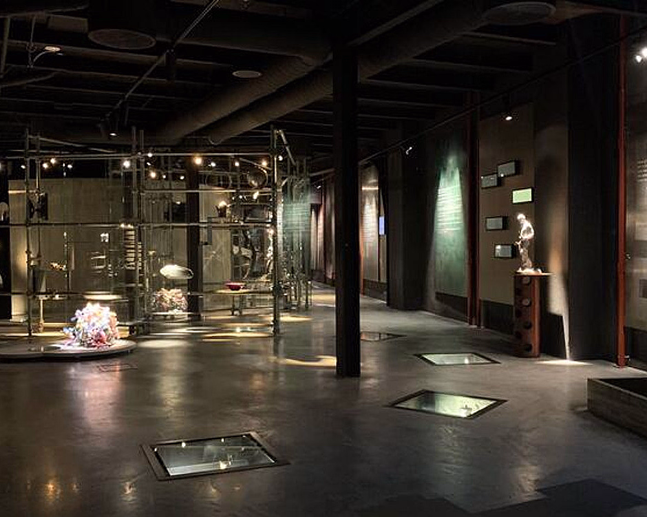 Moderne museumsutstilling med glassmontere, belysning og en blå glassvegg