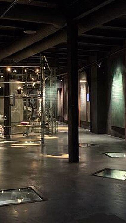 Moderne museumsutstilling med glassmontere, belysning og en blå glassvegg
