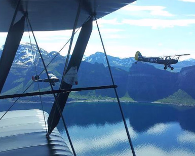To veteranfly i luften over en fjord med fjell i bakgrunnen