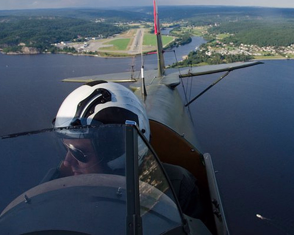 Pilot i cockpit på et småfly over vann og landskap