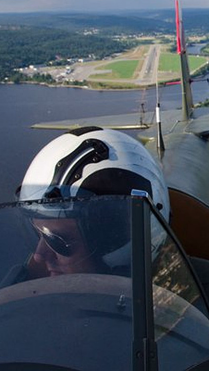 Pilot i cockpit på et småfly over vann og landskap