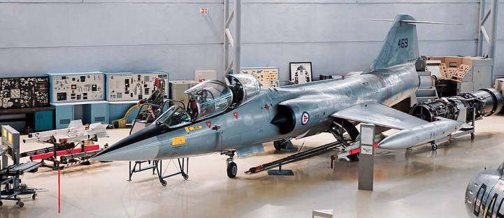 Et grått jagerfly utstilt i en hangar med åpen cockpit og teknisk utstyr i bakgrunnen