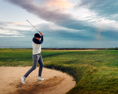 Mann som slår en golfball ut av en sandbunker på en golfbane