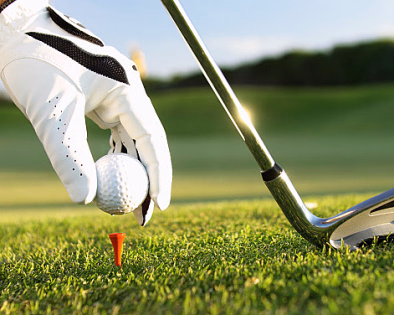 Hånd med hvit golfhanske som plasserer en golfball på en oransje peg på gresset