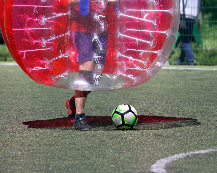 Person i en rød bobleball som spiller fotball på en gressbane