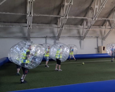Personer i store oppblåsbare plastballer spiller fotball på en innendørs bane