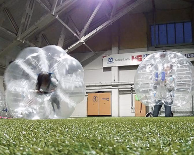 Personer inne i store, gjennomsiktige plastballer på en innendørs fotballbane