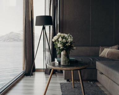 Moderne stue med sofa, lite bord og utsikt over en fjord gjennom store vinduer