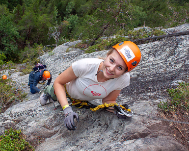 Kvinne med oransje hjelm klatrer i en fjellvegg med via ferrata-utstyr
