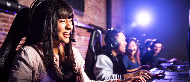 Smilende kvinne med headset som spiller dataspill sammen med andre i et gaminglokale