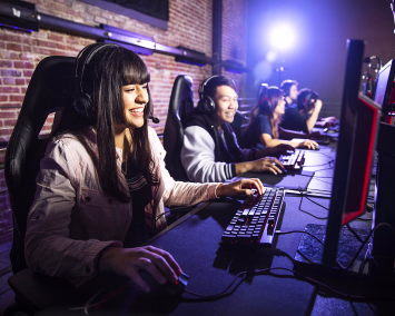 En kvinne med headset som spiller dataspill på en gaming-kafé sammen med andre