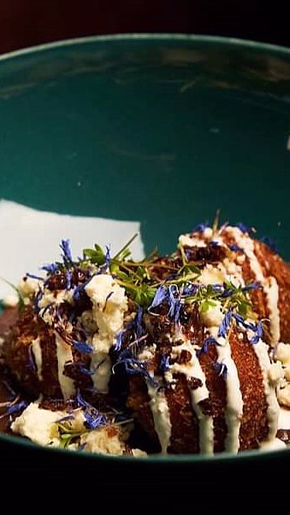 Frityrstekte boller toppet med hvit saus og blå blomster i en grønn bolle