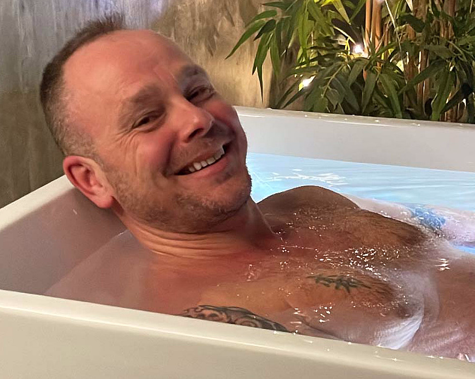 Smilende mann som sitter i et badekar med vann