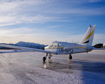 Hvitt småfly med kjennetegn LN-NPO på en islagt rullebane med fjell i bakgrunnen