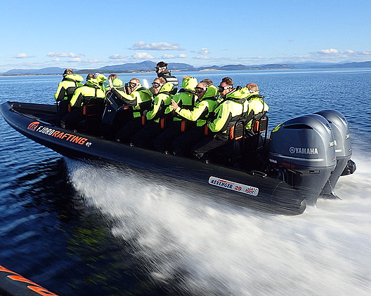 Gruppe i gule dresser på en RIB-båt i fart på fjorden