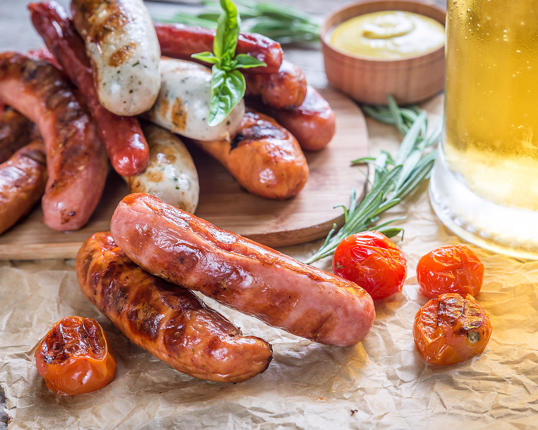 Grillede pølser servert med stekte tomater, urter og et glass lyst øl