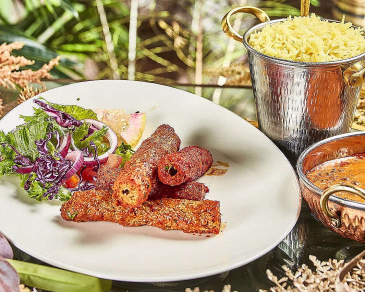Grillede kjøttruller servert med salat, ris i en metallbøtte og en skål med saus