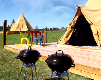 To telt og en treplatting med fargerike stoler og to kulegriller på en gressplen