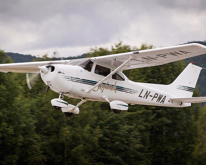 Hvitt småfly med kjennetegn LN-PWA i lav høyde over grønn skog