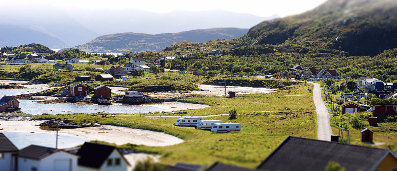 Campingplass med campingvogner og små hytter ved kysten med fjell i bakgrunnen