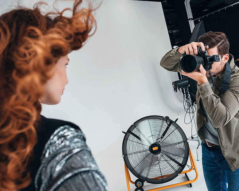 Fotograf tar bilde av en kvinne med rødlig hår i et fotostudio med vifte og lysutstyr
