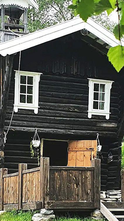 Gammelt stabbur i mørkt tømmer med klokketårn og hvitmalte vinduer