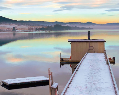 Flytende badstue ved enden av en snødekket brygge i en fjord ved solnedgang