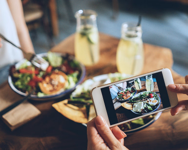 En person tar bilde av lunsjen sin med en mobiltelefon ved et restaurantbord