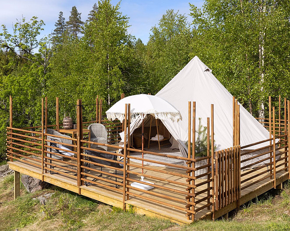 Hvitt glampingtelt på en treplatting med stoler og parasoll omgitt av skog