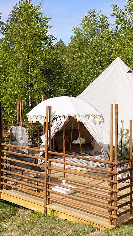 Hvitt glampingtelt på en treplatting med stoler og parasoll omgitt av skog