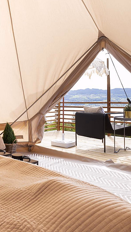 Interiør i et glampingtelt med seng og utsikt til en terrasse med stoler