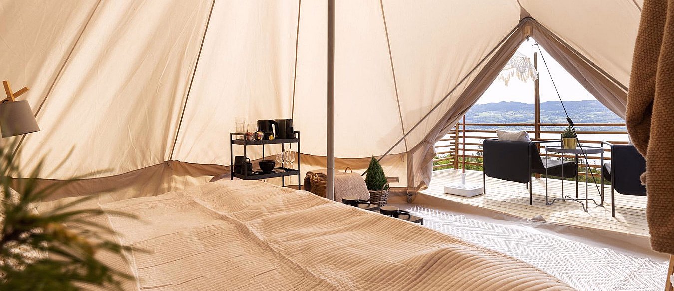 Interiør i et glampingtelt med seng og utsikt til en terrasse med stoler