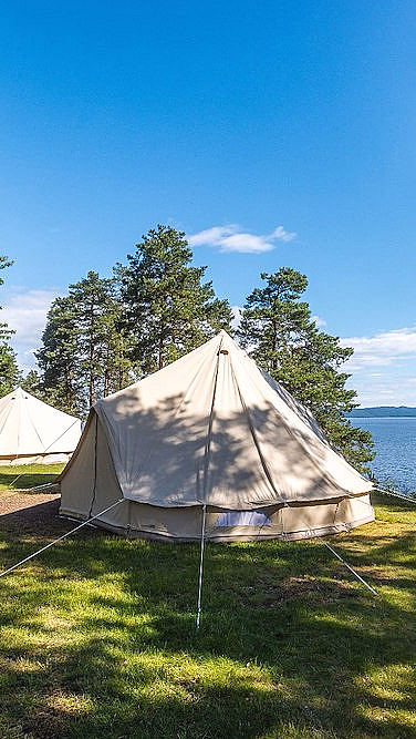 Store glampingtelt på en gressplen ved vannet omgitt av trær