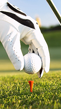 Hånd med hvit hanske plasserer en hvit golfball på en rød peg ved siden av en golfkølle