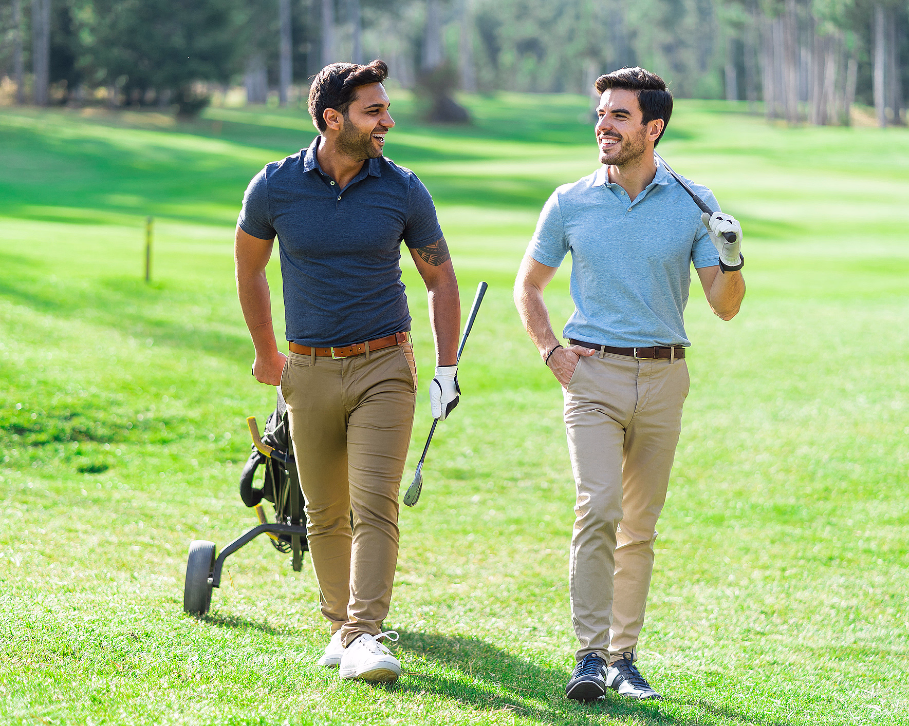 To menn med golfkøller og en golfbag på hjul går over en grønn golfbane