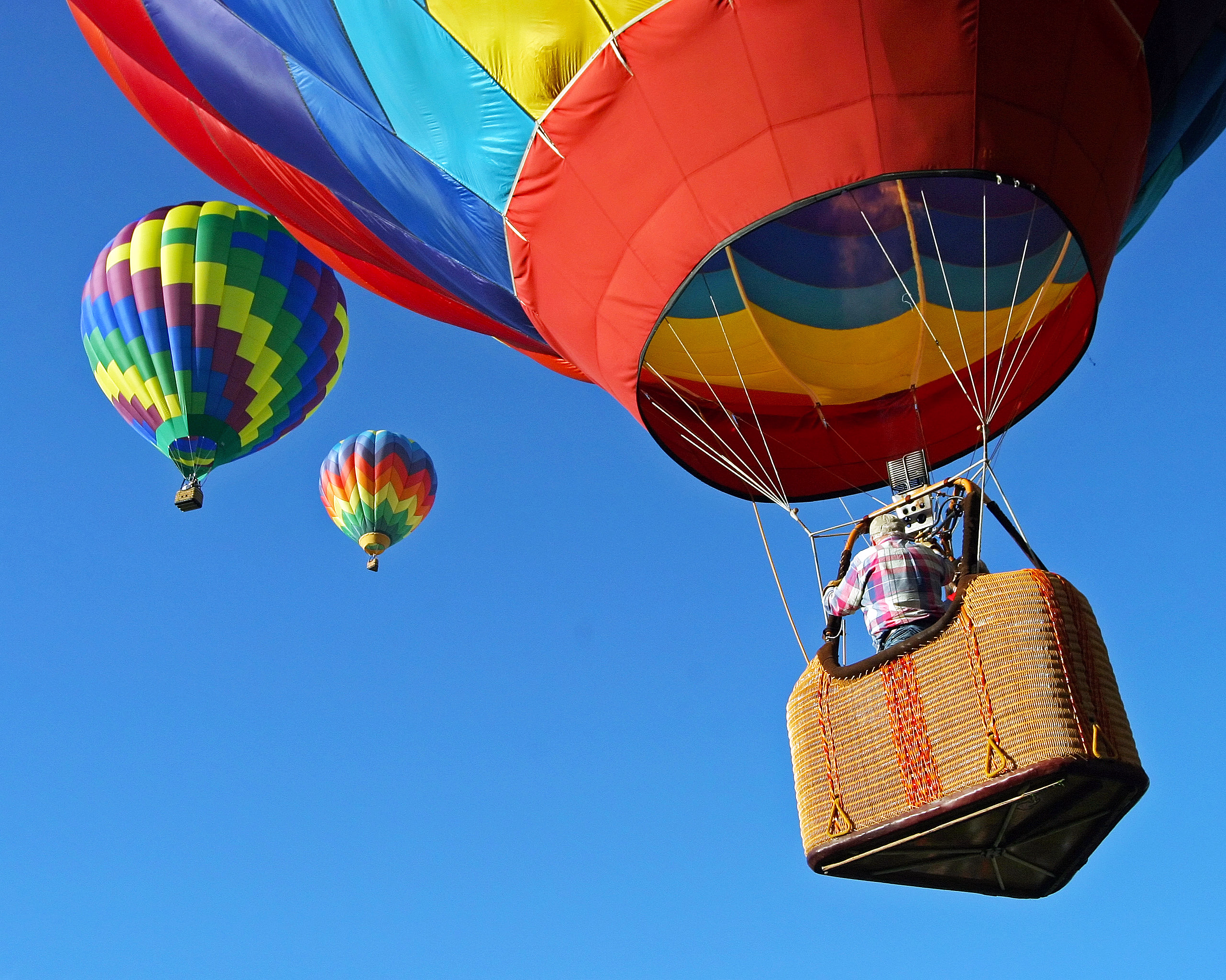 Tre fargerike varmluftsballonger mot en blå himmel med en person i den nærmeste kurven