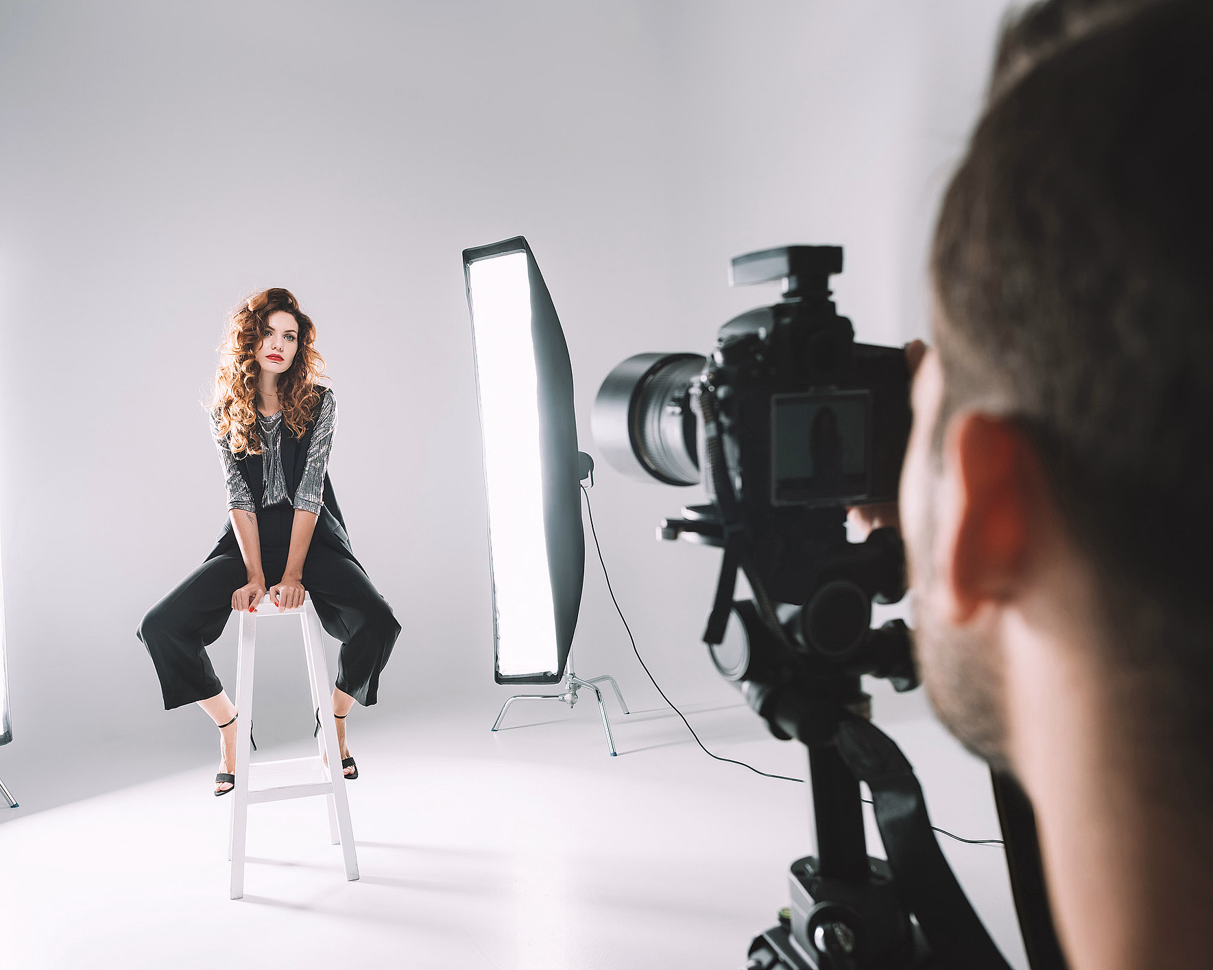 Kvinne med krøllete hår på hvit krakk i et fotostudio med lamper og kamera