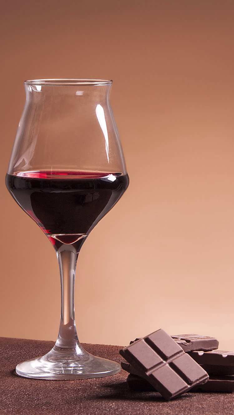 Et glass rødvin ved siden av biter med sjokolade