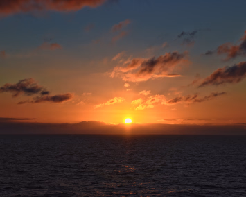 Solnedgang over havet med oransje himmel og skyer