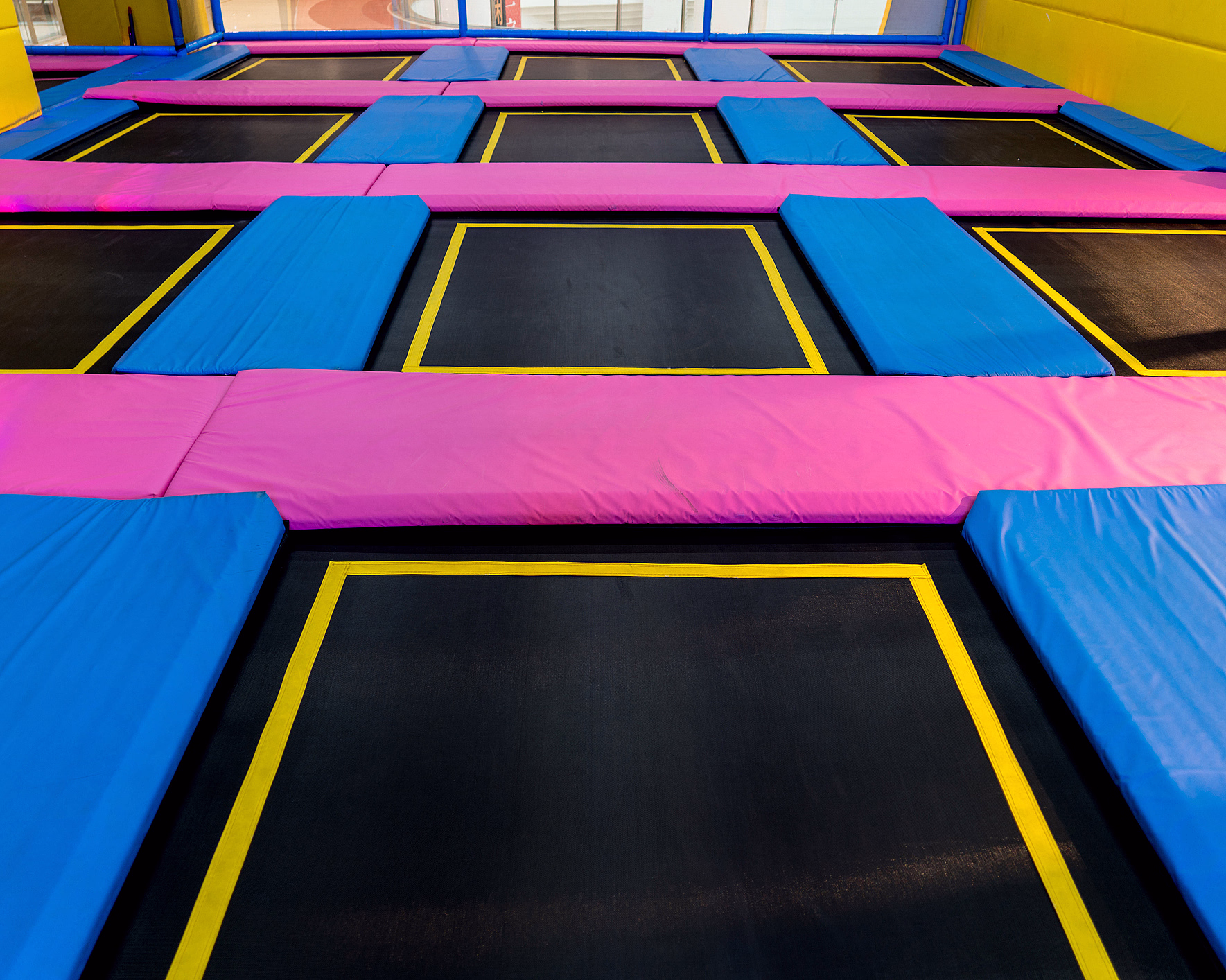 Innendørs trampolinepark med svarte trampoliner og blå og rosa polstringer