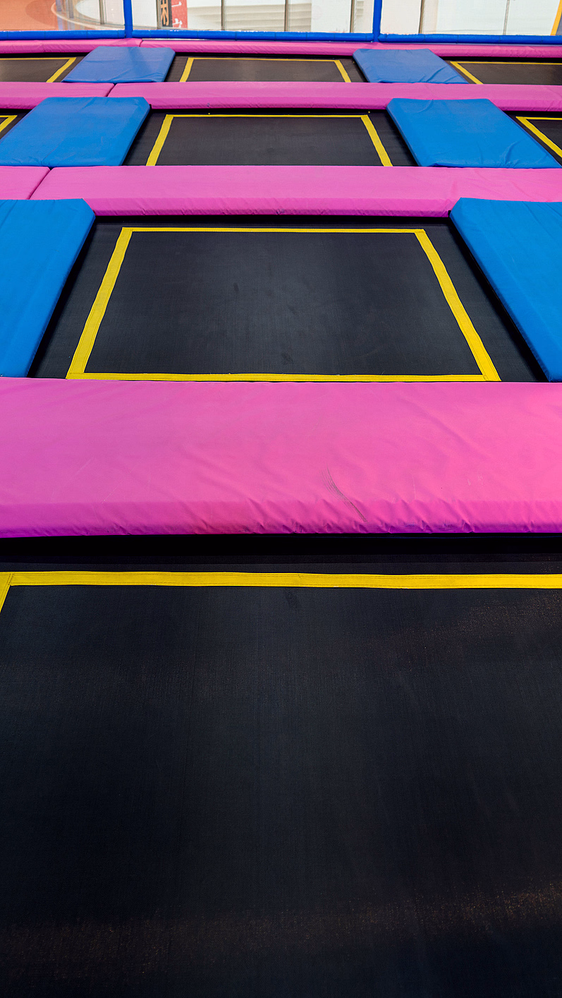 Innendørs trampolinepark med svarte trampoliner og blå og rosa polstringer