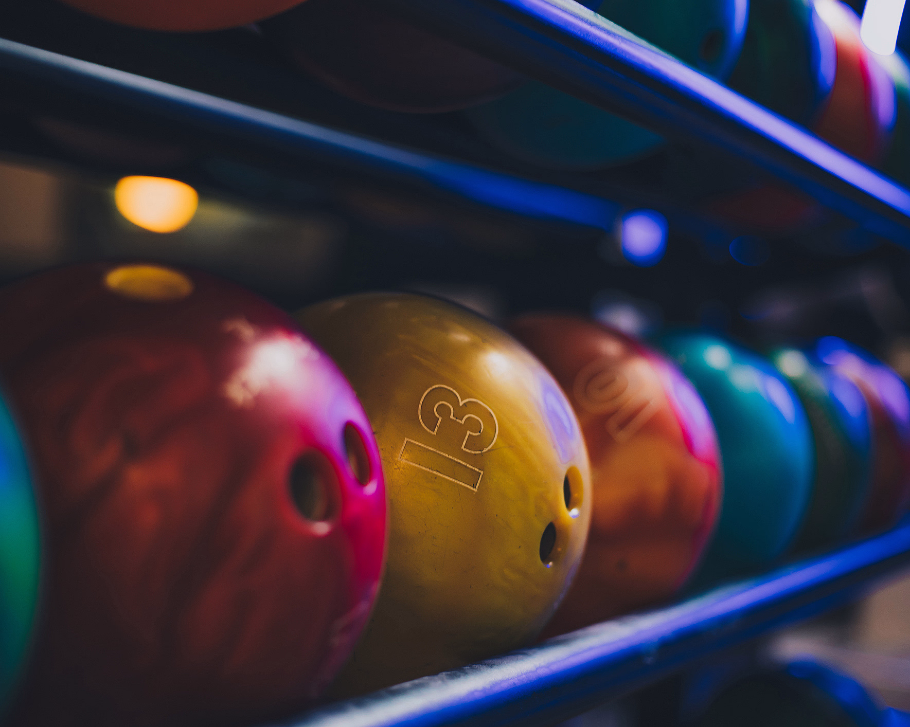 Fargerike bowlingkuler på et stativ i blå belysning med tallet 13 på en gul kule