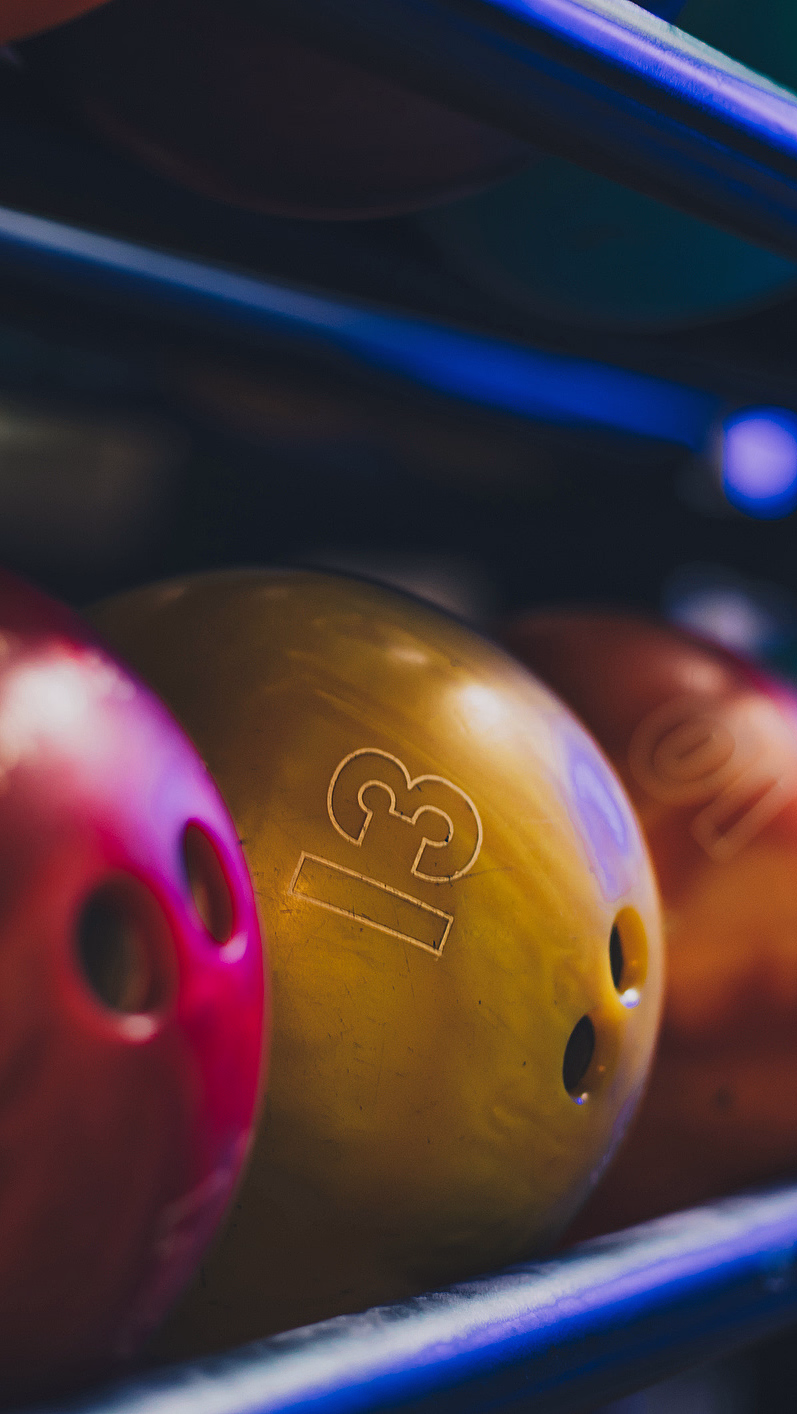 Fargerike bowlingkuler på et stativ i blå belysning med tallet 13 på en gul kule