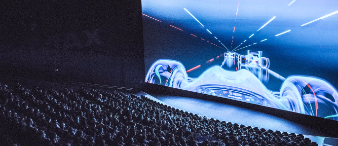 Publikum i en kinosal ser på en futuristisk racingscene på et IMAX-lerret
