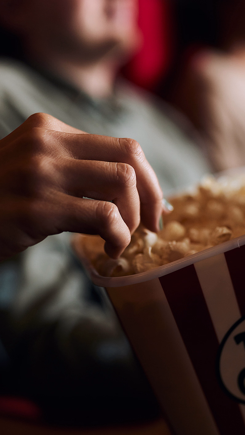 Hånd som tar popcorn fra et rød- og hvitstripet beger med teksten Popcorn