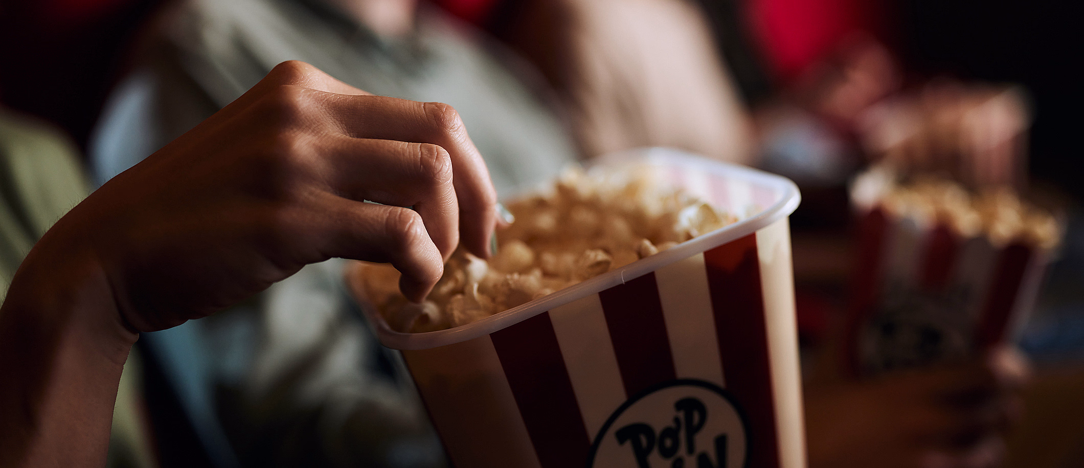 Hånd som tar popcorn fra et rød- og hvitstripet beger med teksten Popcorn