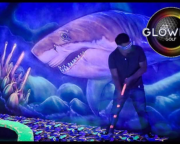 Person spiller minigolf i et neonbelyst rom med undervannstema og Glowing Golf-logo