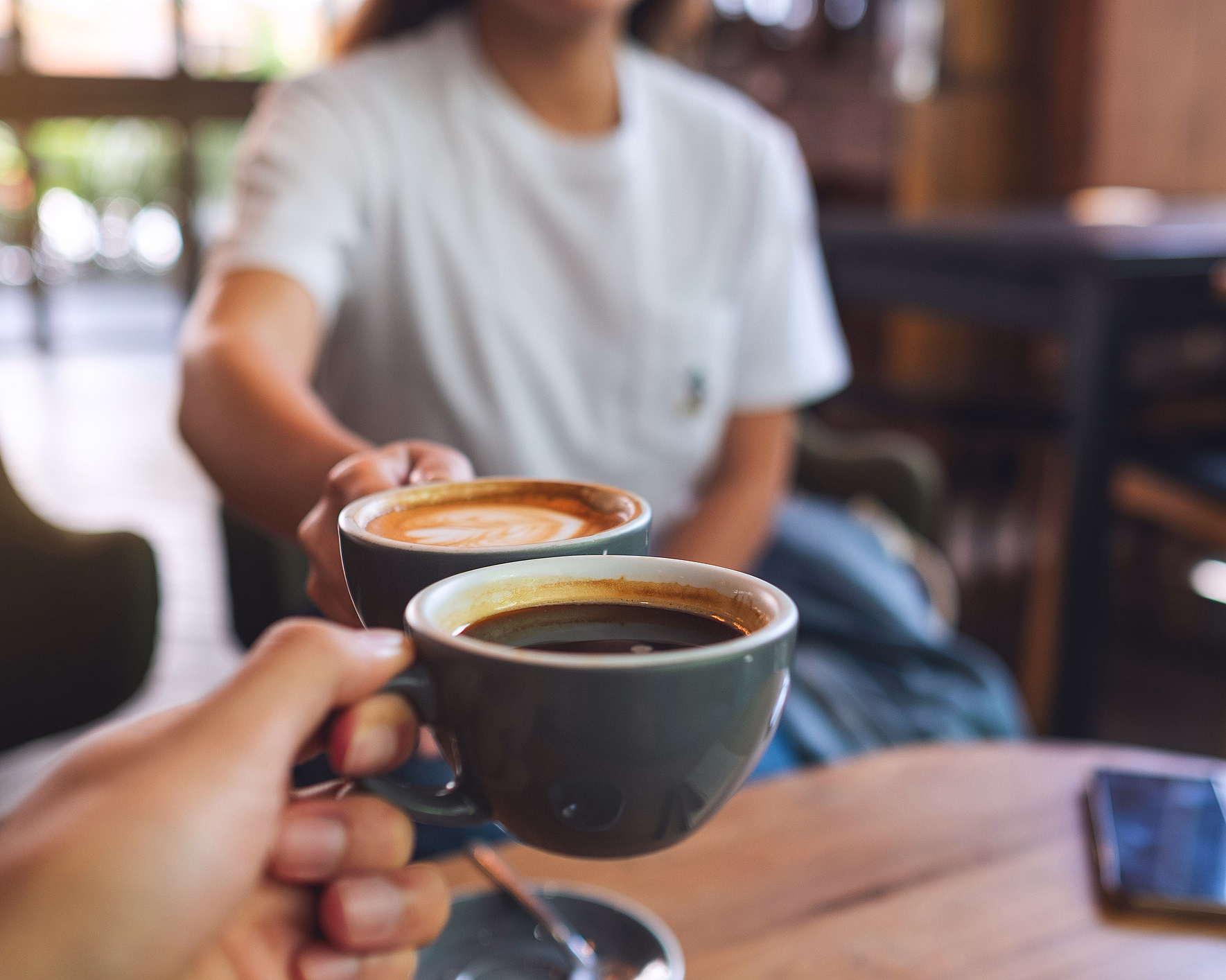 To personer skåler med kaffekopper over et trebord med en smarttelefon