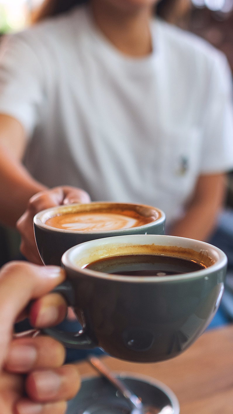 To personer skåler med kaffekopper over et trebord med en smarttelefon